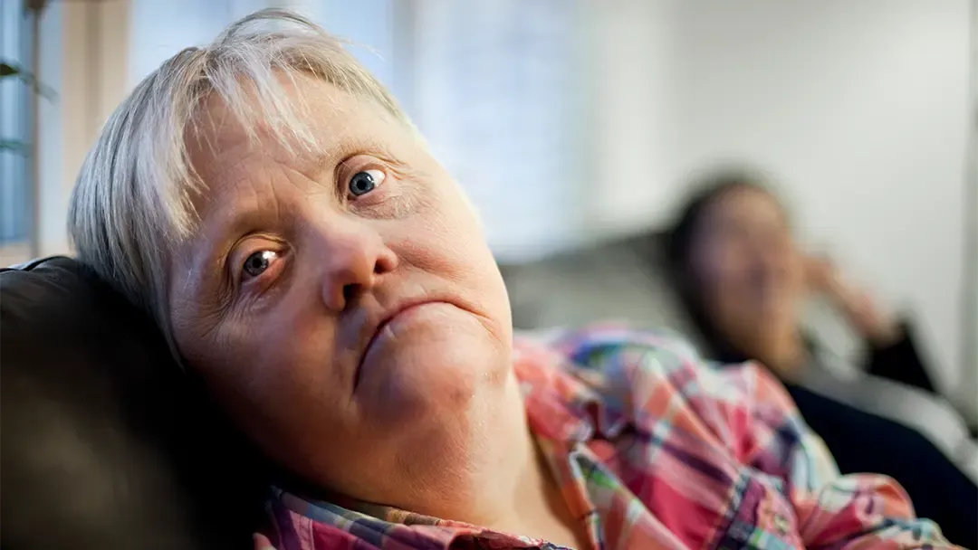 Frau mit Down Syndrom sitzt auf einer Couch